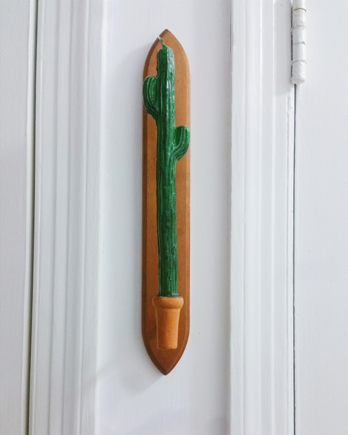 Wooden candlestick holder from thrift store between two doors in a hallway with a cactus candle