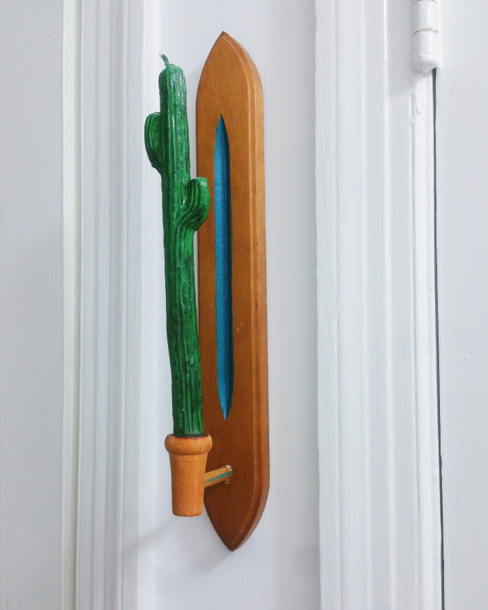 Wooden candlestick holder from thrift store between two doors in a hallway with a cactus candle and painted center detail