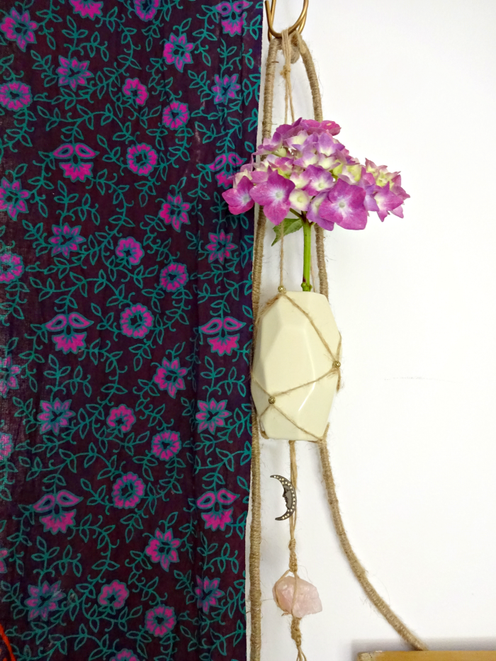 hydrangea in hanging handmade vase beside floral tapestry curtain