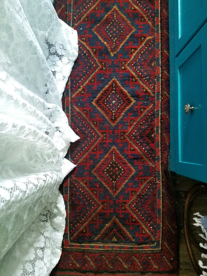 Dark blue and burgundy area rug in the bathroom with lace curtains and blue vanity